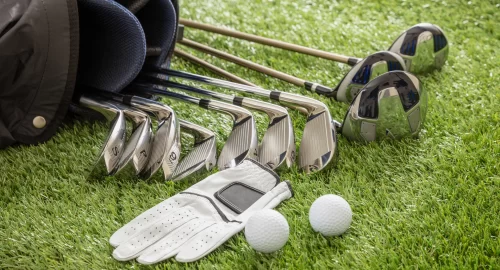 Golf bag laying on its side with golf clubs, a glove and two golf balls