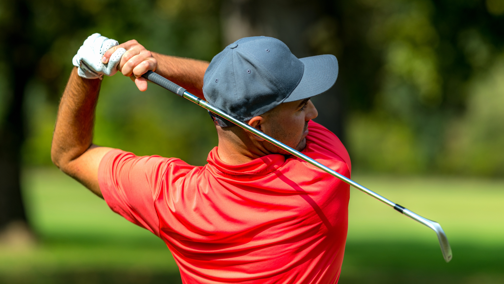 Golfer in red polo and a hat on that just finished a swing