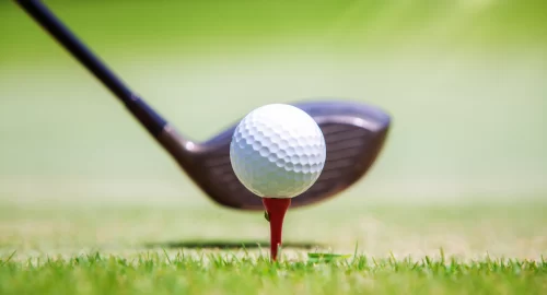 Golf ball on tee with the head of a golf club right behind it