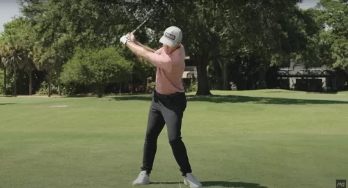 Photo of a man swinging a golf club mid-swing with an alignment stick on the ground.