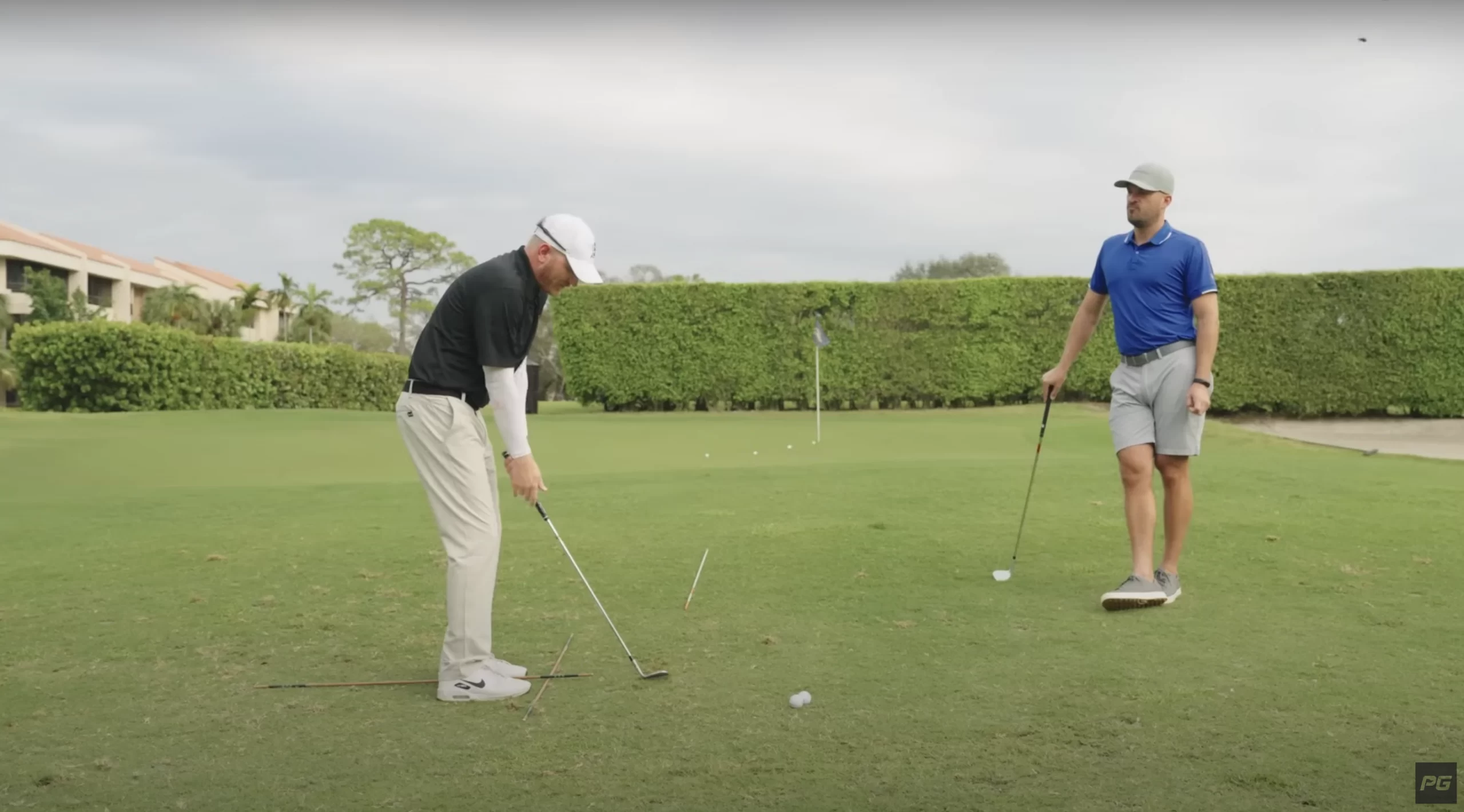 Two Performance Golf coaches on the green, one on the left is in the golf short game setup while the other is on the right, leaning on his golf club watching on.