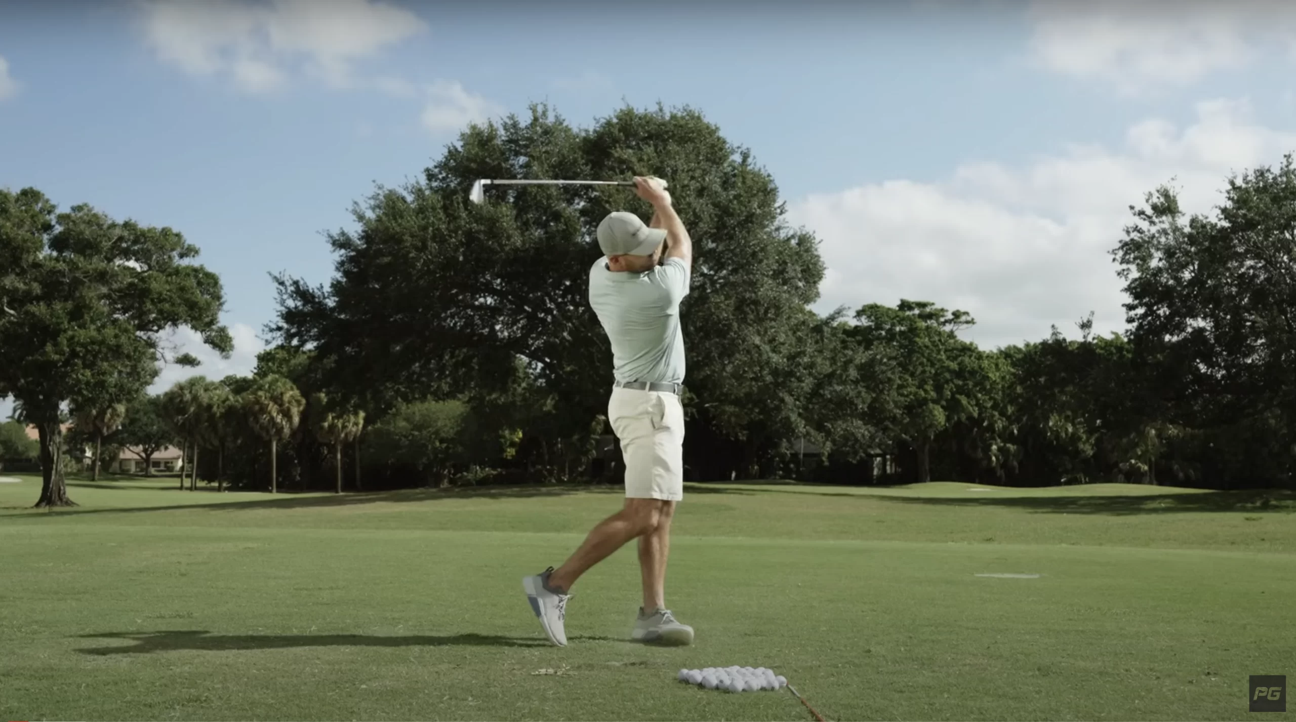 Performance Golf Coach Eric Cogorno on the golf course, mid swing with the golf club above his head and a pile of golf balls on the ground in front of him.